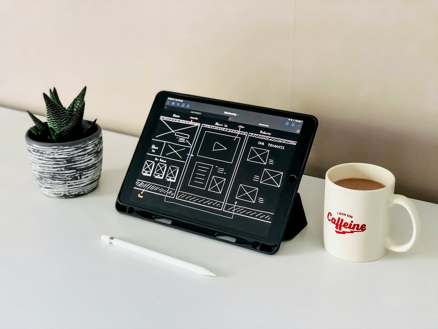 iPad con wireframe di sito web, Apple Pencil e caffè su una scrivania bianca.